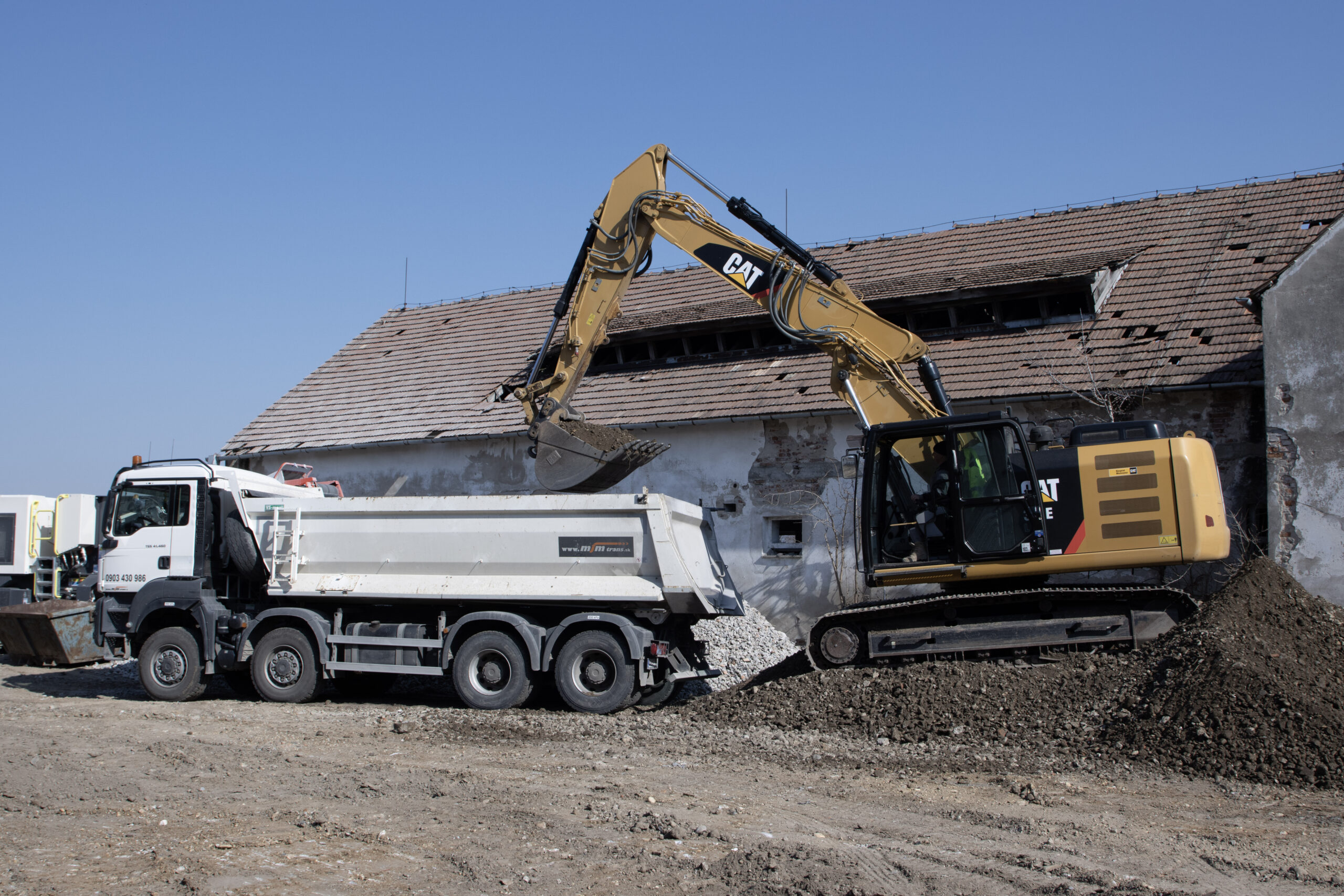 Nakladanie odpadu – excavátor CAT a sklápač MJM Trans Excavátor CAT 316 nakládá stavebný odpad na sklápač MJM Trans pri demolácii budovy