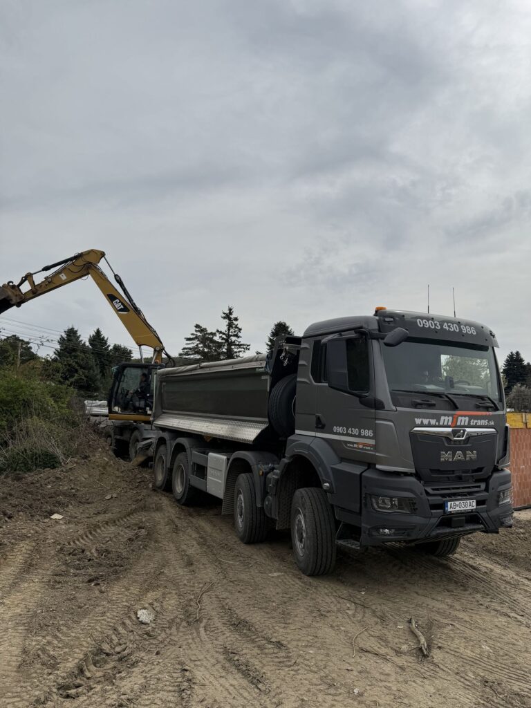 Sivý sklápač MAN 8×8 pri nakládke na stavbe