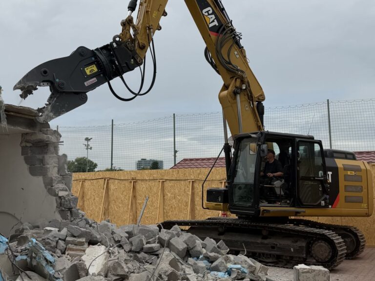 Pásové rýpadlo CAT 320E s drviacimi kliešťami pri demolácii objektu