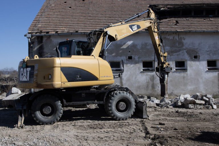 Kolesové rýpadlo CAT M316D s kladivom pri objekte